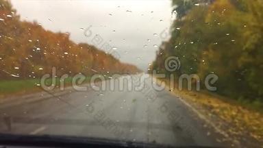 汽车上路沥青旅行.. 秋天美丽的风景林，雨滴在玻璃车上模糊的背景缓慢